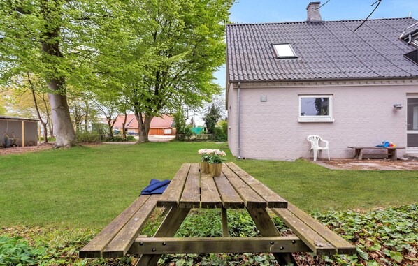 A wooden picnic table with a bench, surrounded by a well-maintained lawn and a large tree.
