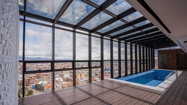 Piscina no terraço com vista para a cidade, grandes janelas e um deque de madeira.