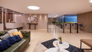 Um lobby moderno com um sofá verde, uma mesa de centro de mármore e uma receção com painéis de vidro.