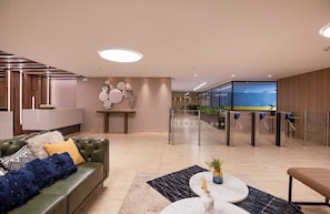 Eine moderne Lobby mit einem grünen Sofa, einem Marmortisch und einer Rezeption mit Glasverkleidung.