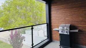 Un balcon avec vue sur les arbres et un barbecue.