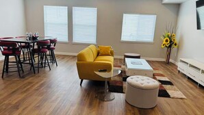 Un salon moderne avec un canapé jaune, une table basse en verre et un coin repas avec des chaises rouges.