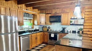 A kitchen with wooden cabinets, stainless steel appliances, and a checkered floor mat. - Cozy Perrysburg Cabins - Modern 2 Bedroom with Large Loft & Sleep#Bed! (Perrysburg)