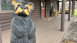 A wooden cabin with a porch, a bear sculpture, and a Christmas wreath. - Cozy Perrysburg Cabins - Modern 2 Bedroom with Large Loft & Sleep#Bed! (Perrysburg)