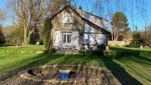 A rustic stone building with a sloped roof, a small porch, and a pond in the foreground. - RIVERSIDE CHARACTER HOUSE WITH OUTBUILDING (Ménilles)