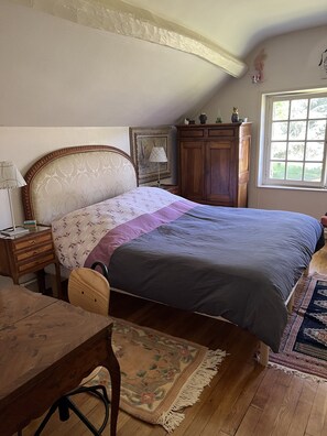 A bedroom with a bed, wooden furniture, a nightstand, a desk, a chair, a window, and a door.