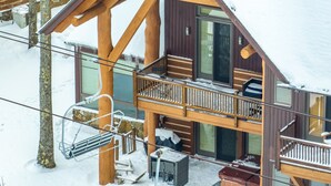 Una cabaña de madera con balcón, un telesilla y un techo cubierto de nieve.