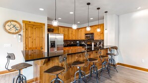 Cocina moderna con armarios de madera, un refrigerador de acero inoxidable, microondas y una isla grande con taburetes de bar.