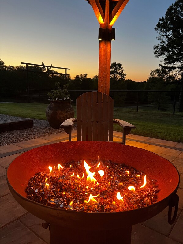 Una chimenea con una silla y una mesa de madera cerca, ubicada en un patio al aire libre.