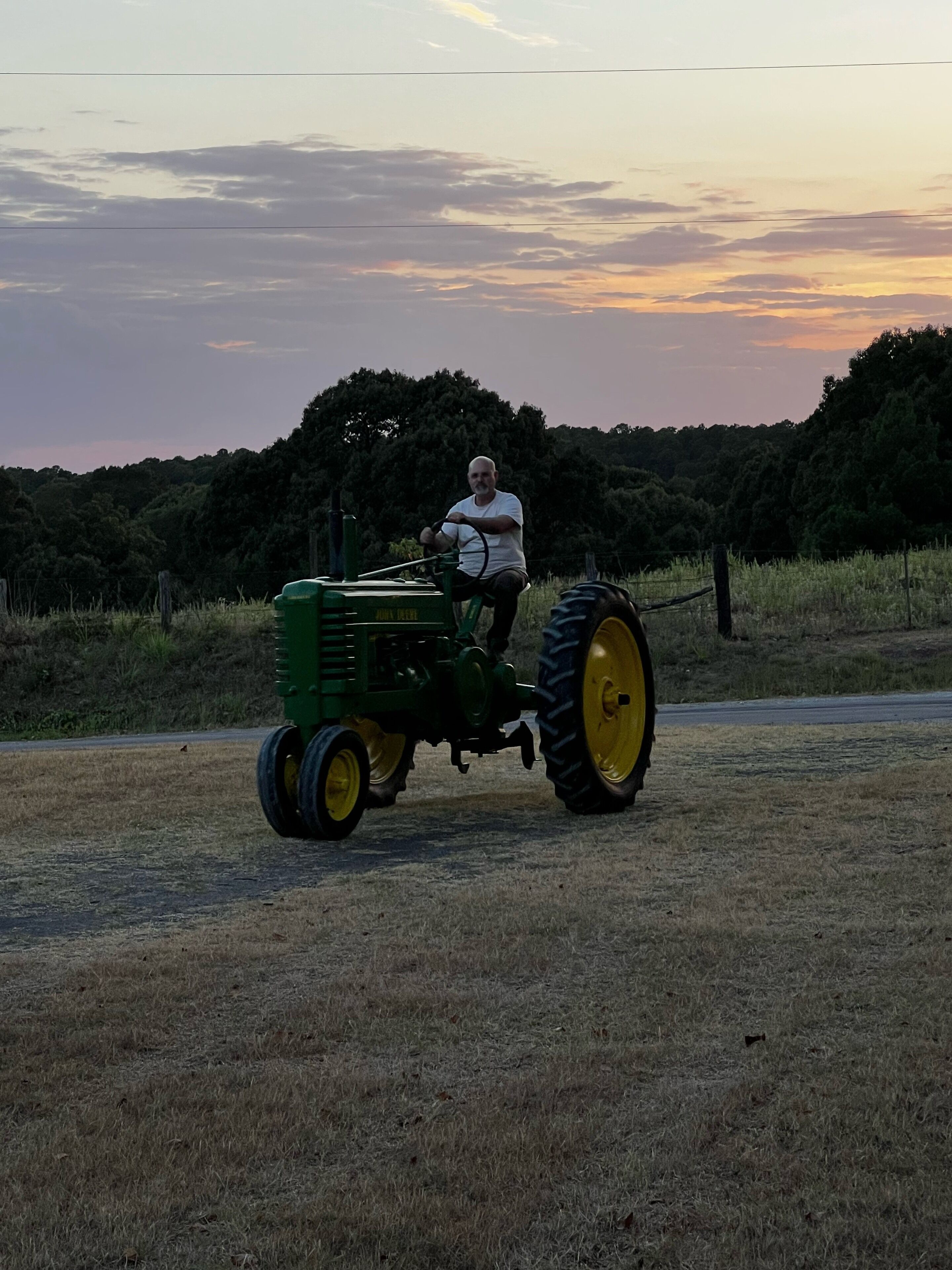 A person driving a green tractor on a rural road.