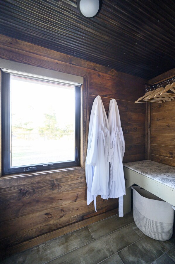 L'intérieur d'un chalet en bois, avec une fenêtre, un banc et un porte-vêtements.