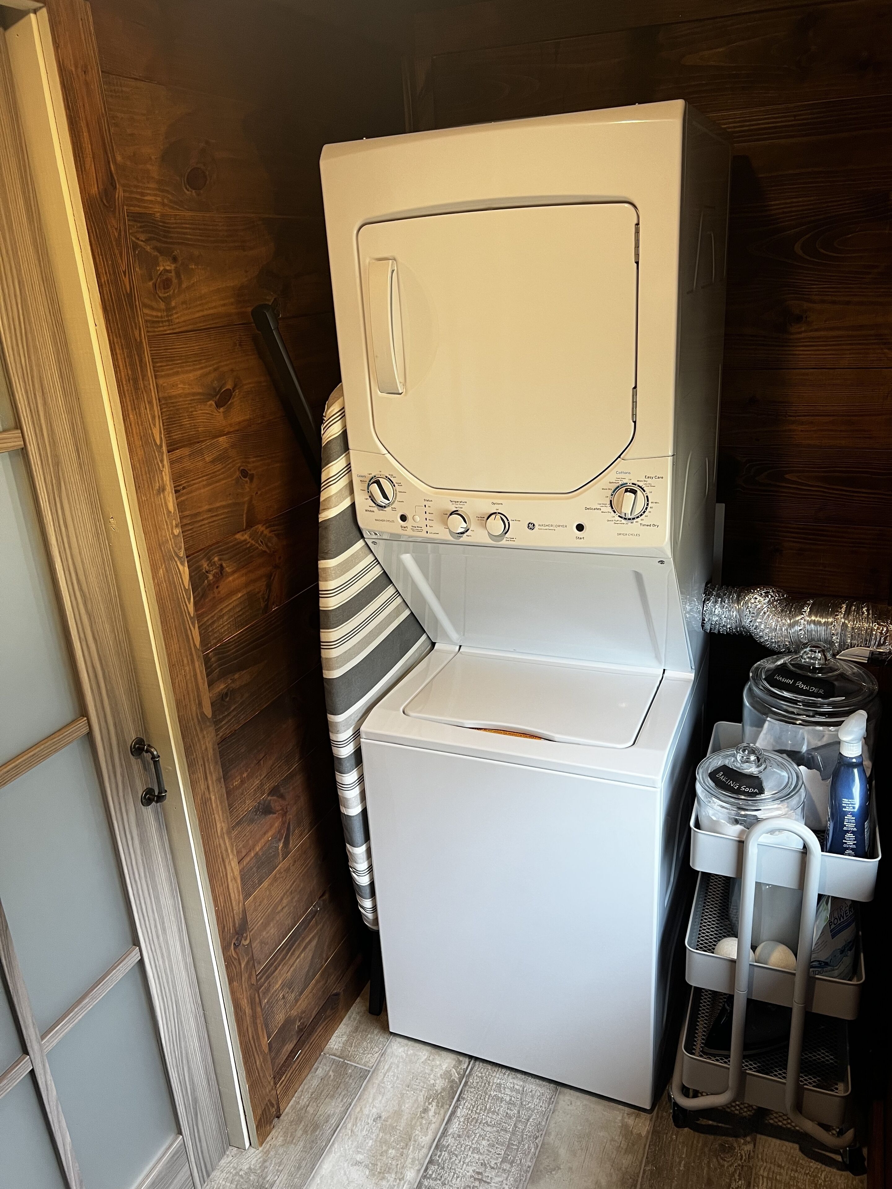 A compact laundry room with a front-loading washer and dryer, a striped towel, and a shelf with cleaning supplies.
