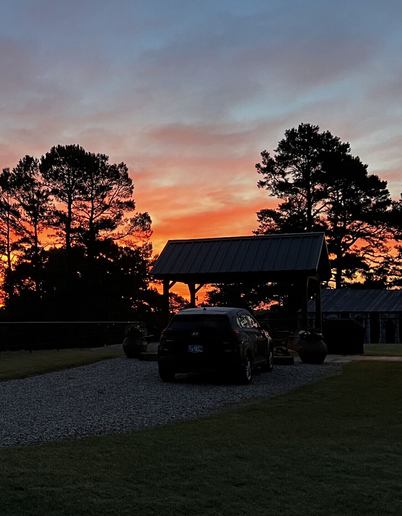 A car parked in front of a building with a covered patio area, surrounded by trees and a sunset sky.