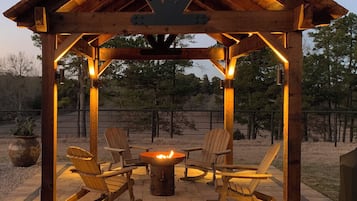 Relax in a serene gazebo with a central fire pit, surrounded by Adirondack chairs on a paved patio.
