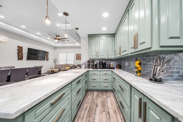 A modern kitchen with green cabinets, a marble countertop, and a dining area with a sofa and chairs.