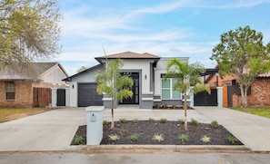 A modern two-story house with a garage, a driveway, and a landscaped front yard with small trees and shrubs.