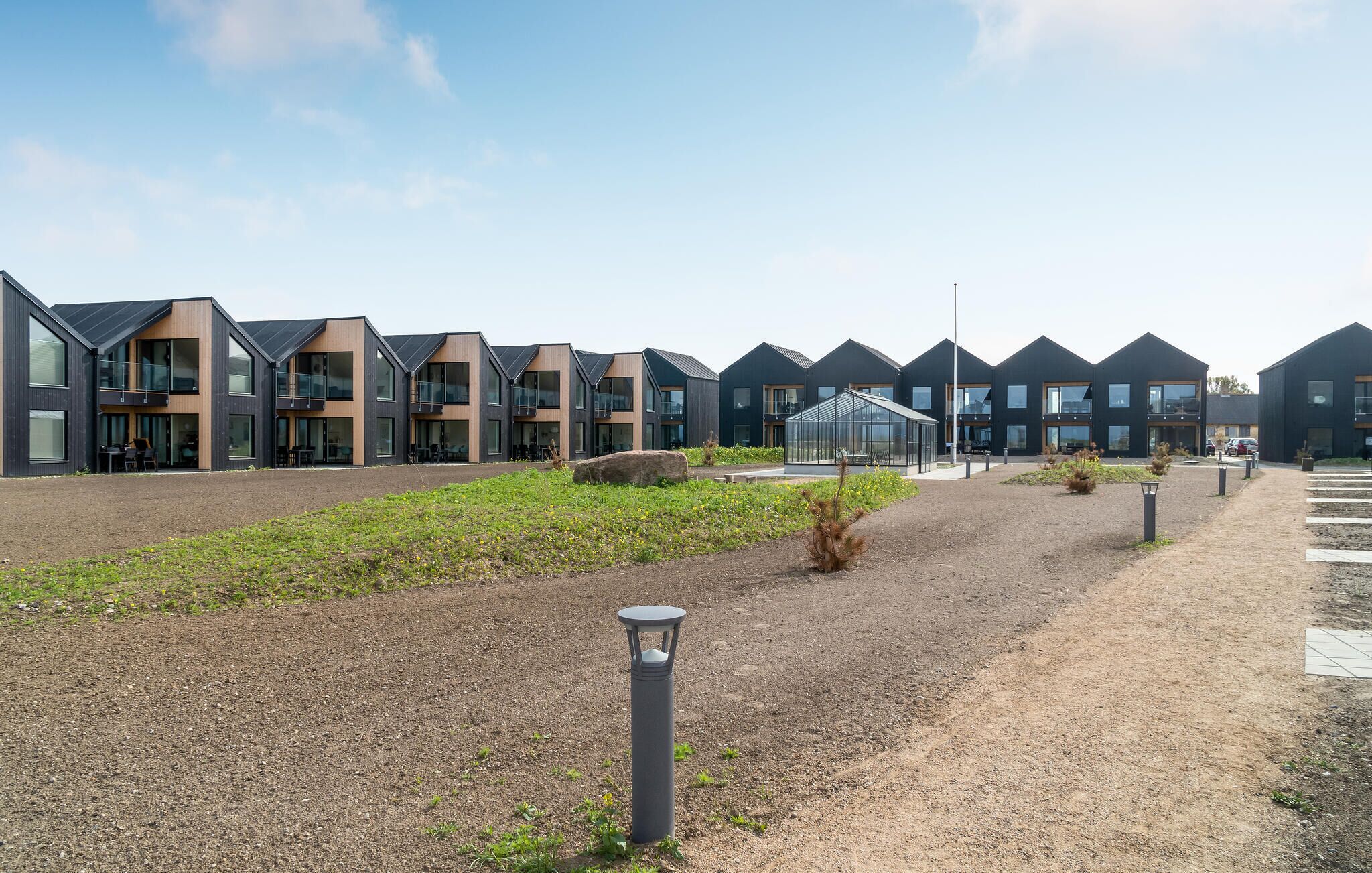 A row of modern, dark-colored buildings with large windows and a greenhouse structure in the middle.