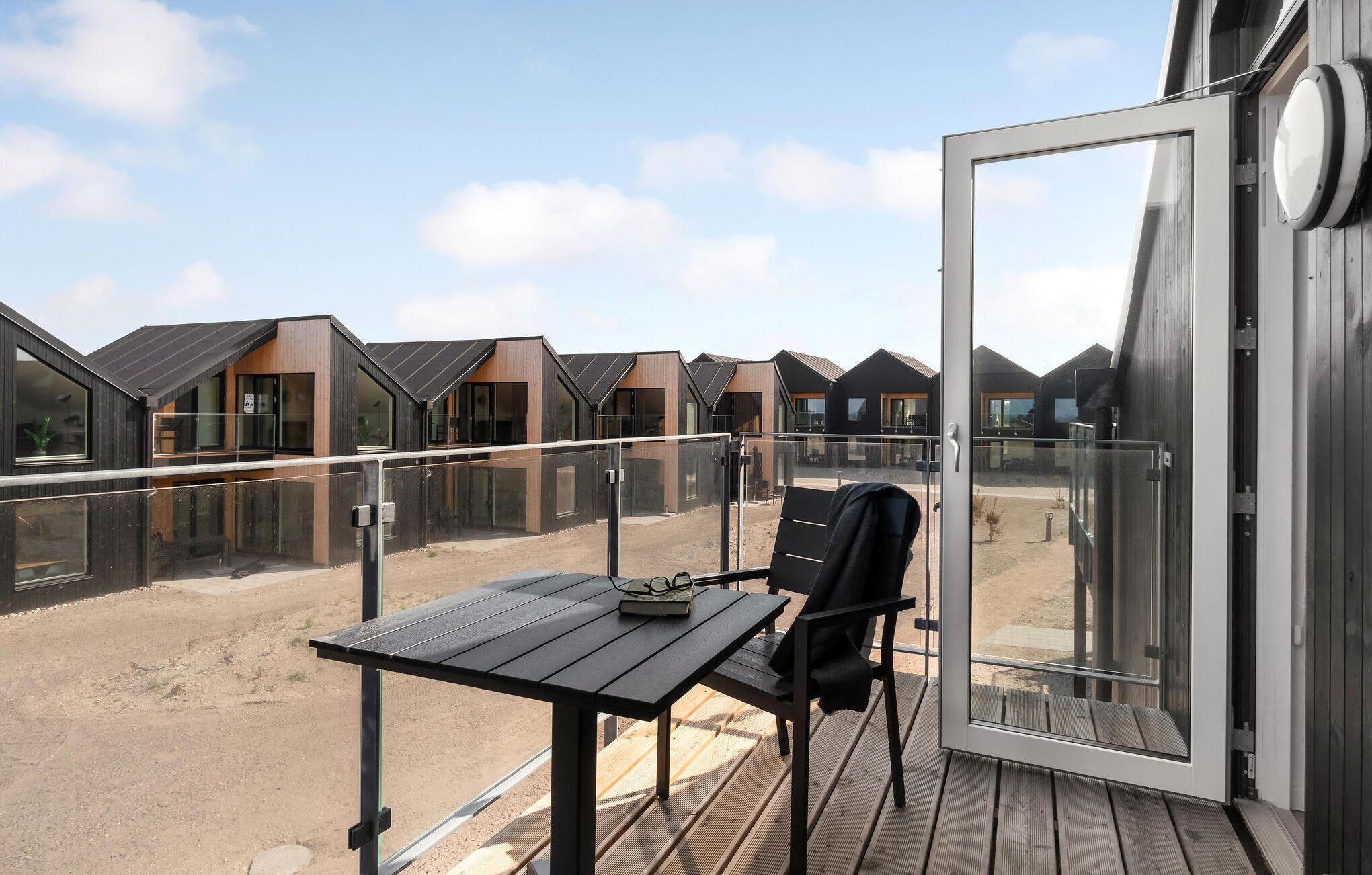 A balcony with a table and chair, overlooking a row of modern buildings with large windows.