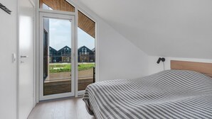 Une chambre avec une grande porte-fenêtre coulissante donnant sur un balcon, un lit avec une couverture à rayures et une tête de lit en bois.