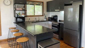 Une cuisine moderne dotée d’un îlot central, de tabourets de bar, d’un réfrigérateur, d’une cuisinière et d’une fenêtre donnant sur un espace verdoyant.