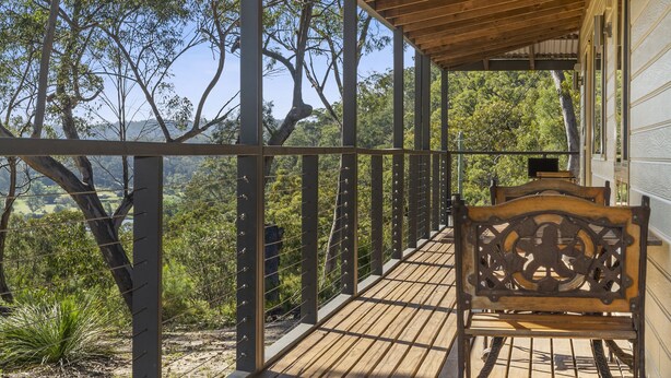 Une terrasse en bois avec un banc, entourée de rampes en métal et d’arbres.