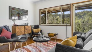 Un salon moderne comprenant un canapé, des fauteuils, une table basse et une grande fenêtre donnant sur un paysage arboré.