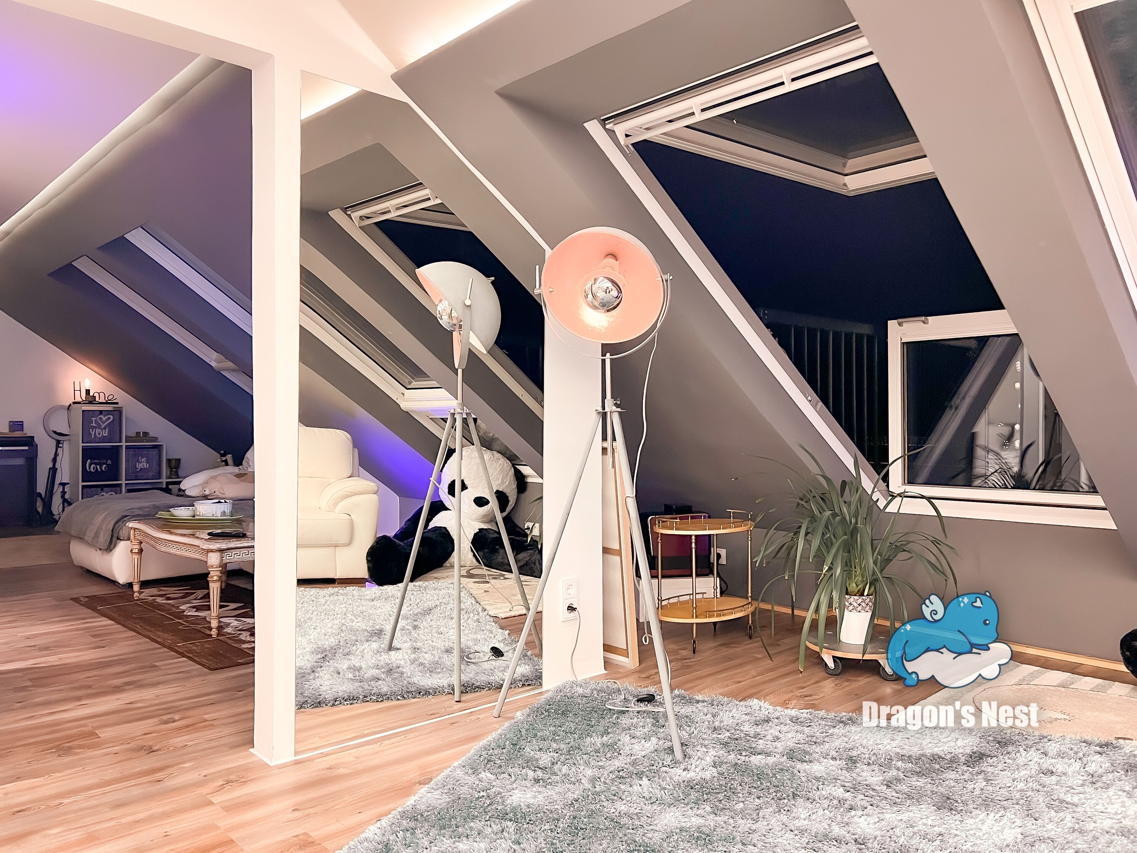 Una camera da letto mansardata accogliente, con soffitto spiovente, una grande finestra, una lampada da terra e un soffice peluche a forma di panda.