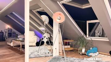 Una camera da letto mansardata accogliente, con soffitto spiovente, una grande finestra, una lampada da terra e un soffice peluche a forma di panda.