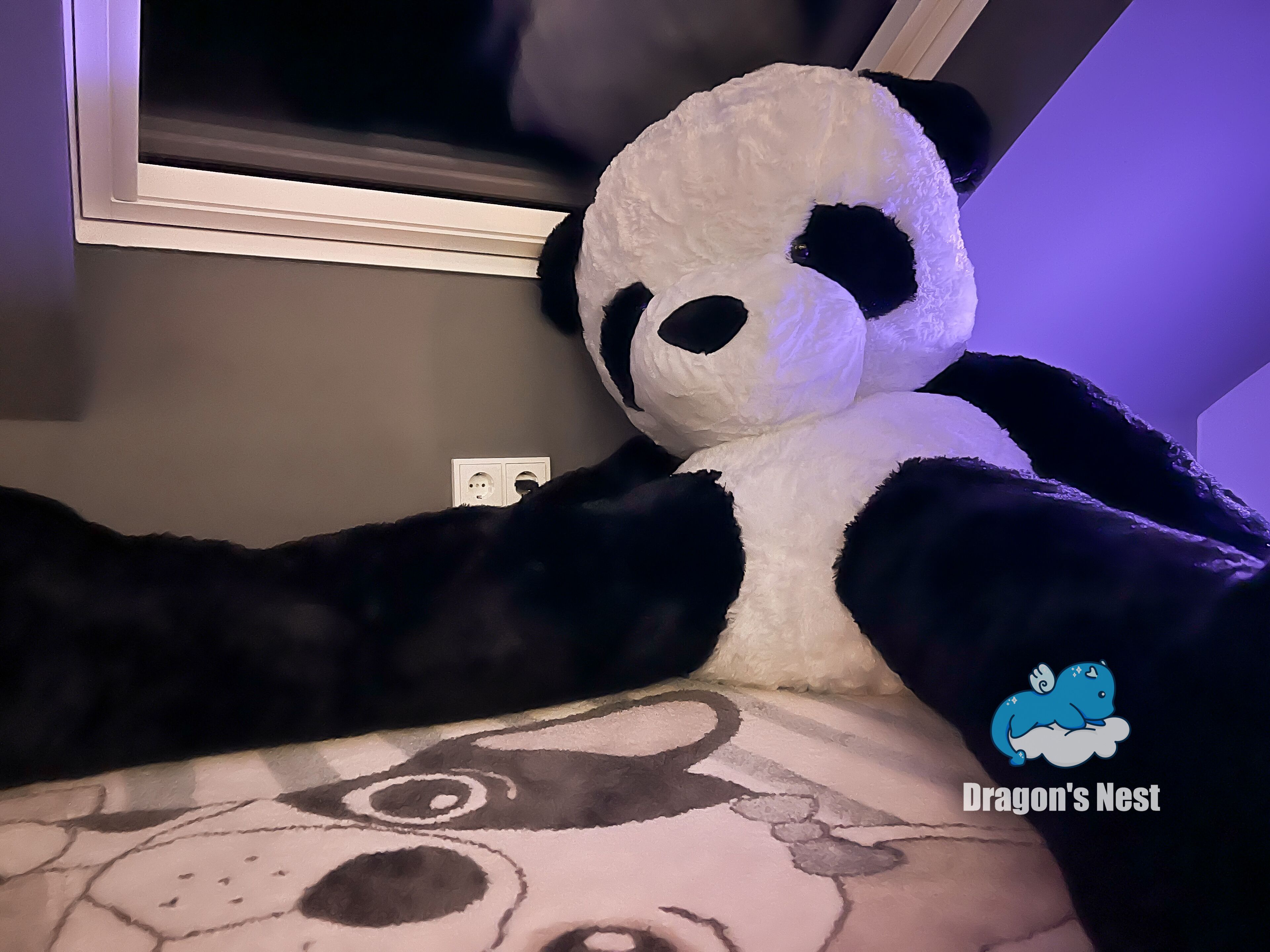Ein großes Plüschpanda auf einem Bett mit einem gemusterten Kopfkissen.