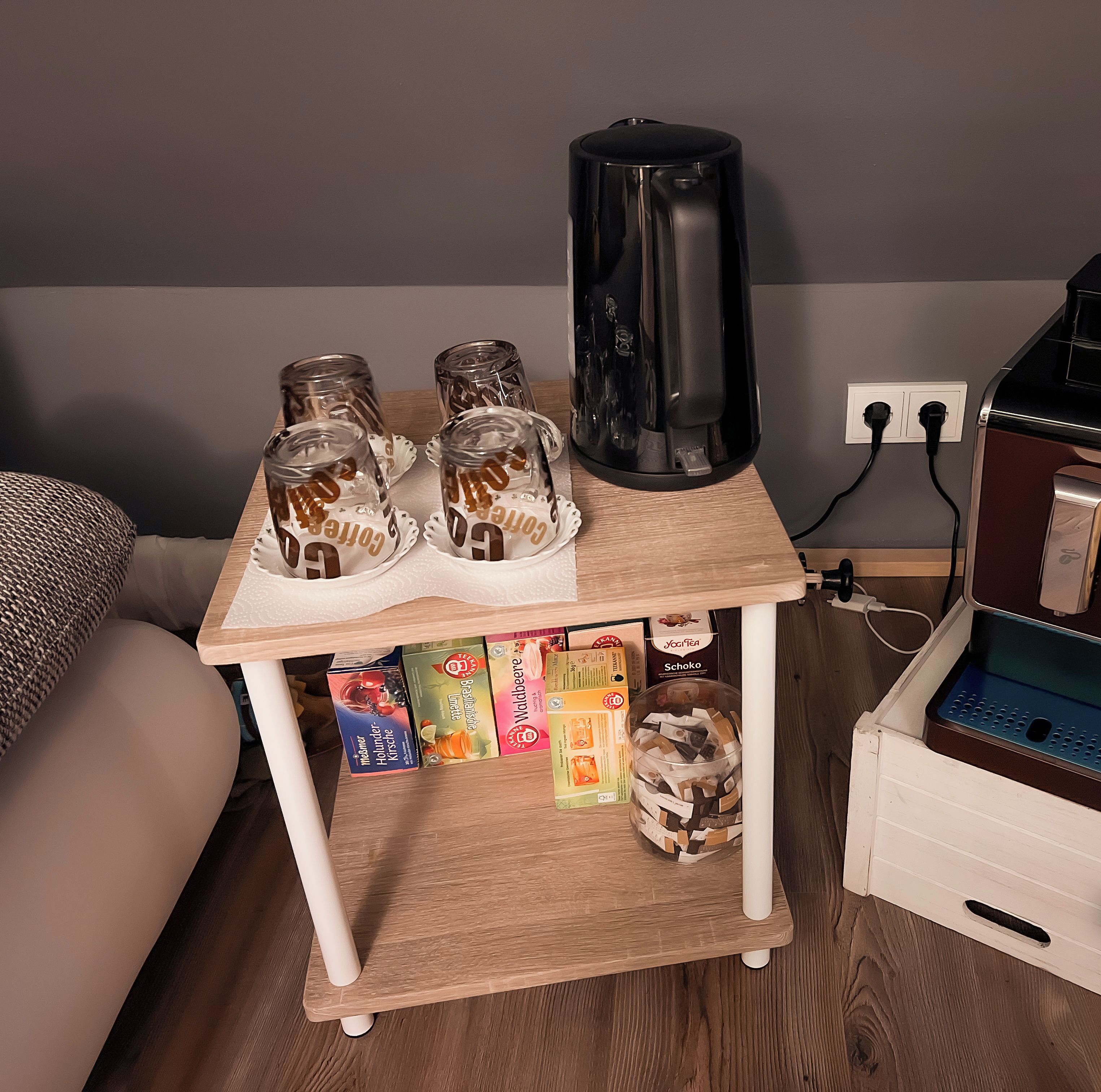 Una máquina de café sobre una mesa de madera con base blanca, un enchufe y un cable de carga.