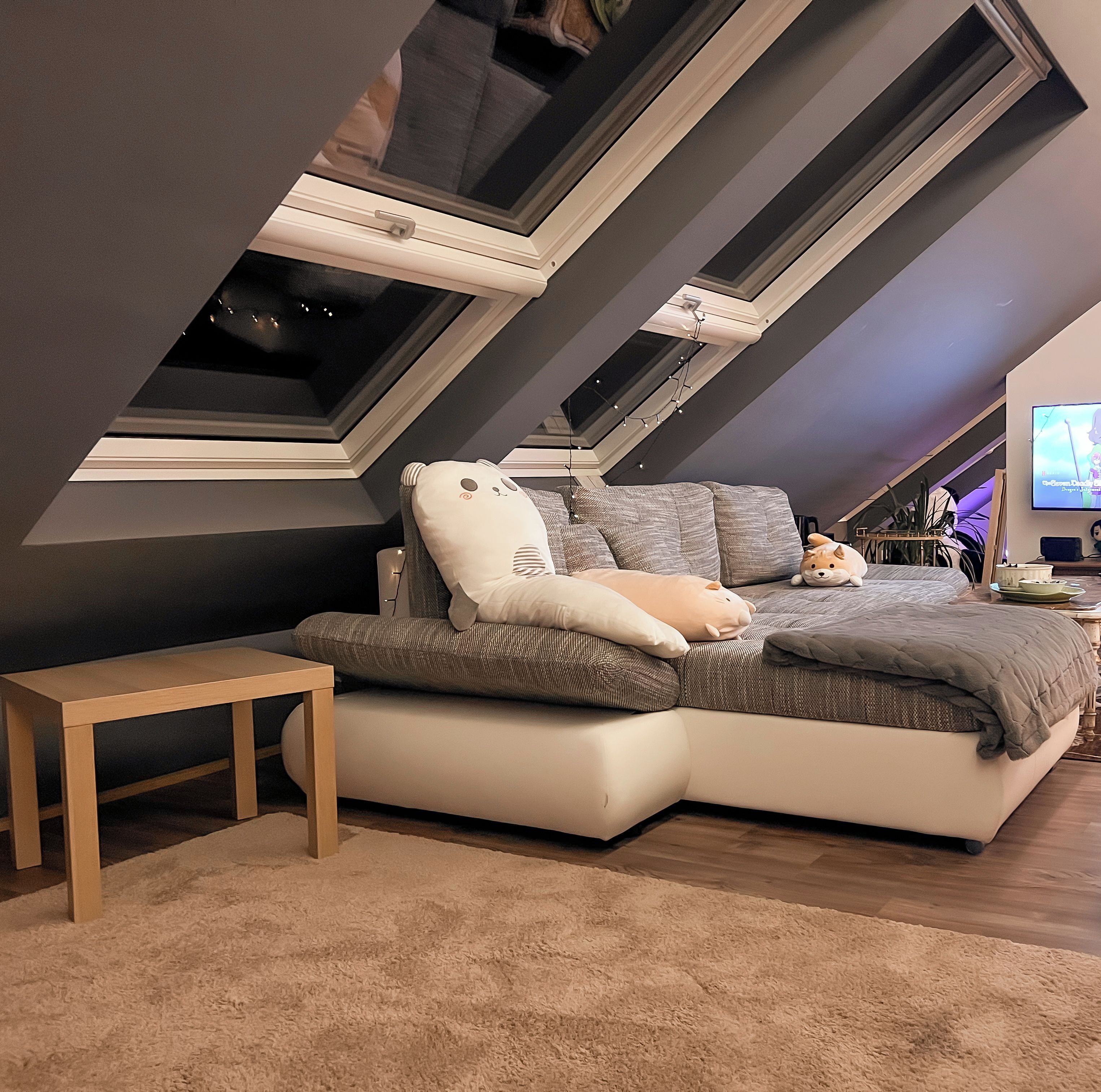 A modern loft bedroom with a sloped ceiling, a large bed, a TV, and a small desk.