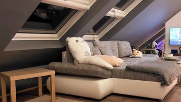 A modern loft bedroom with a sloped ceiling, a large bed, a TV, and a small desk.