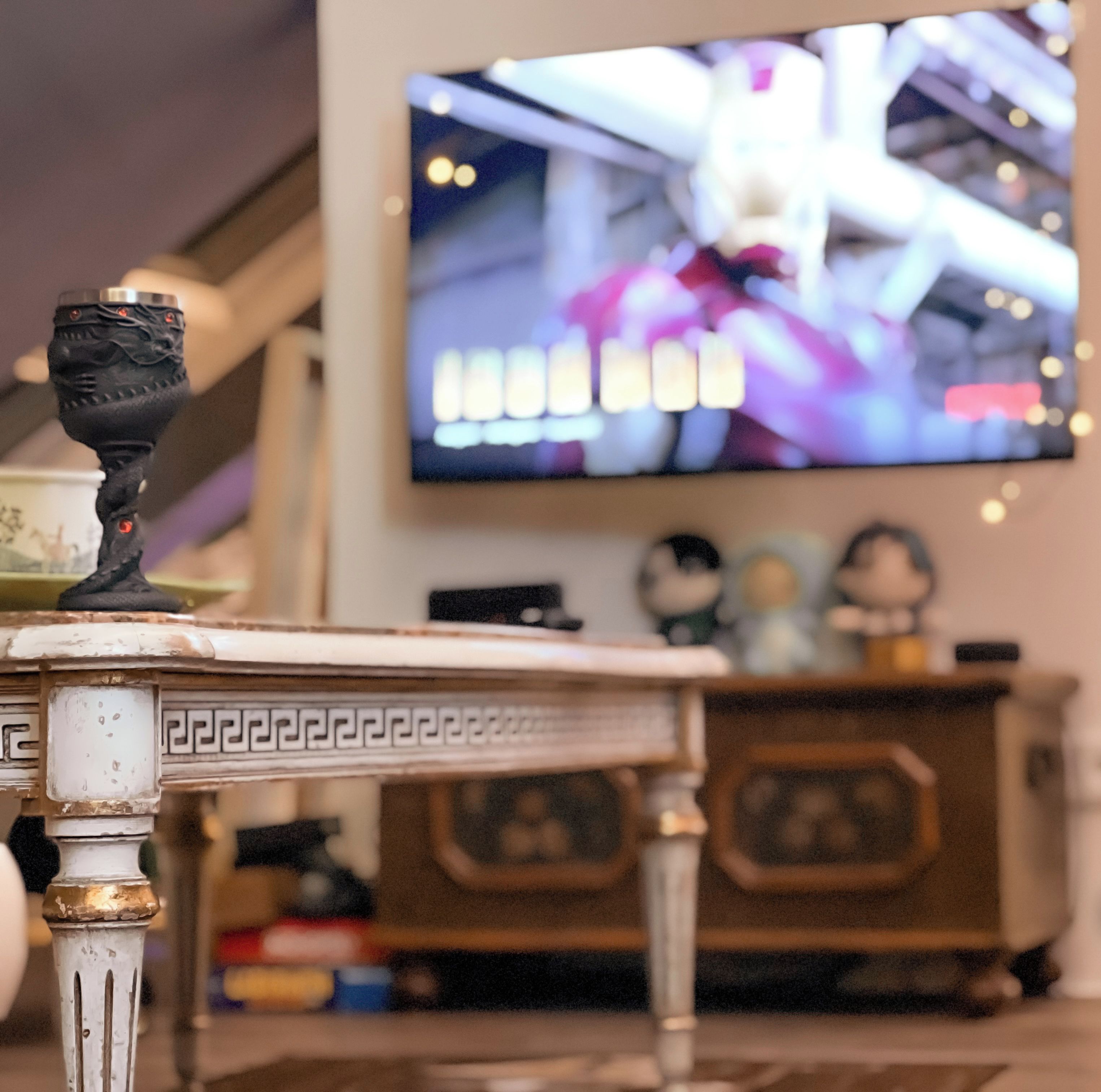 Ett vardagsrum med en tv som hänger på väggen, ett dekorativt bord och ett skåp med små figurer.