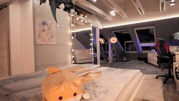 Una camera da letto con un letto, un grande peluche, una scrivania con una sedia e una mensola a muro con oggetti decorativi.