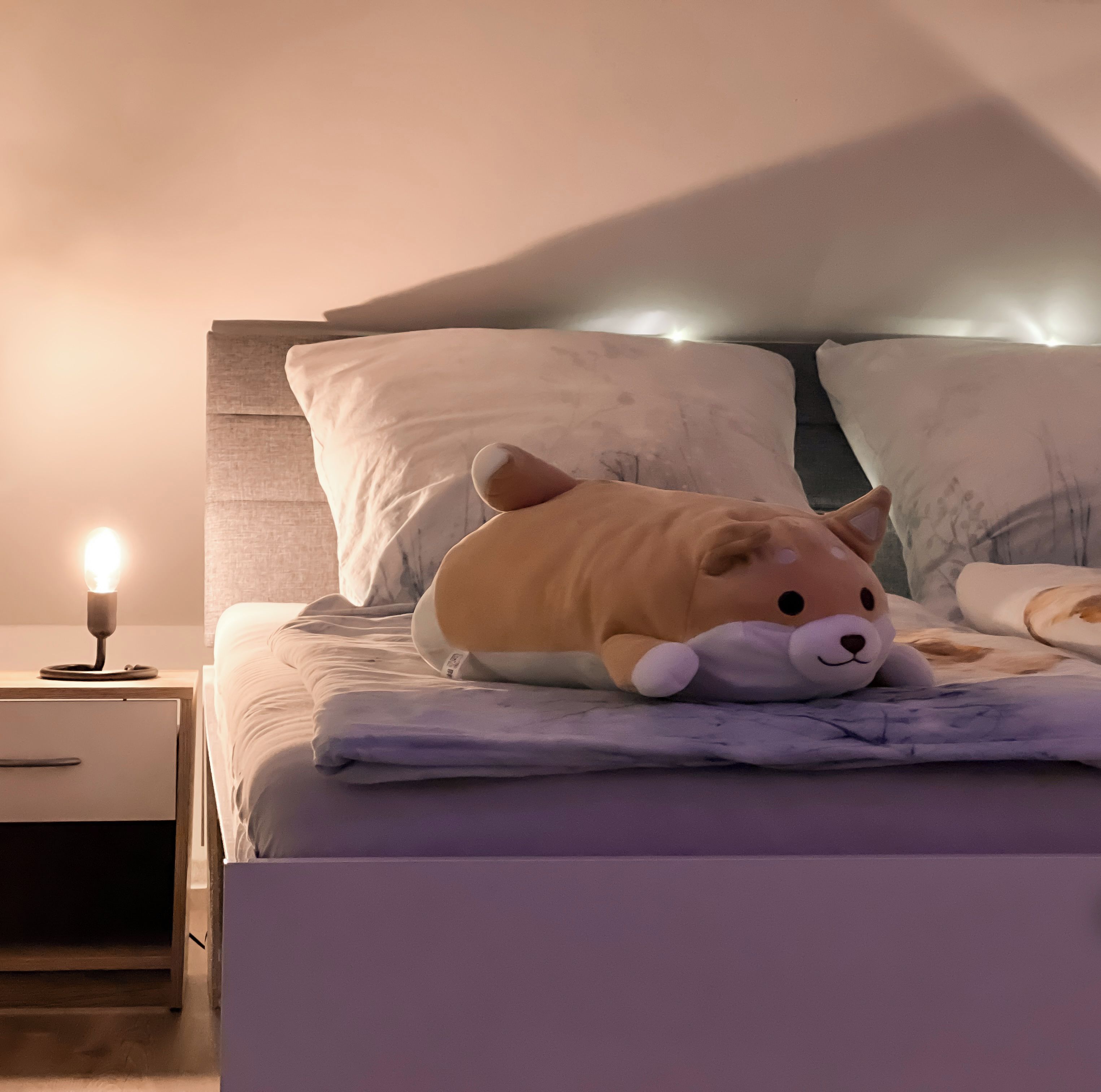 A bed with a plush toy, pillows, and a bedside lamp.