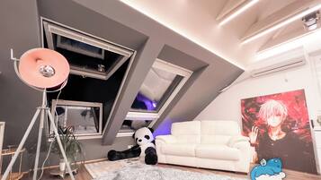 A modern living room with a white sofa, a large window, a panda plush toy, and a poster on the wall.
