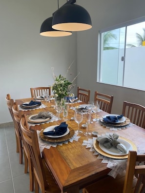 A dining table set for eight with wooden chairs, lace tablecloth, and black pendant lighting.