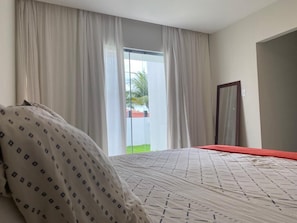 A hotel room with a bed, a large window with curtains, and a view of the outdoors.