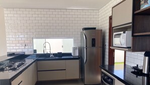 A compact kitchen with a stainless steel refrigerator, a built-in microwave, and a gas stove. - Barra do Jacuípe - House with 3 bedrooms, 1 of which is a suite. (Jacuípe)