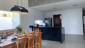 A modern kitchen with white brick walls, a black island, and wooden dining chairs. - Barra do Jacuípe - House with 3 bedrooms, 1 of which is a suite. (Jacuípe)