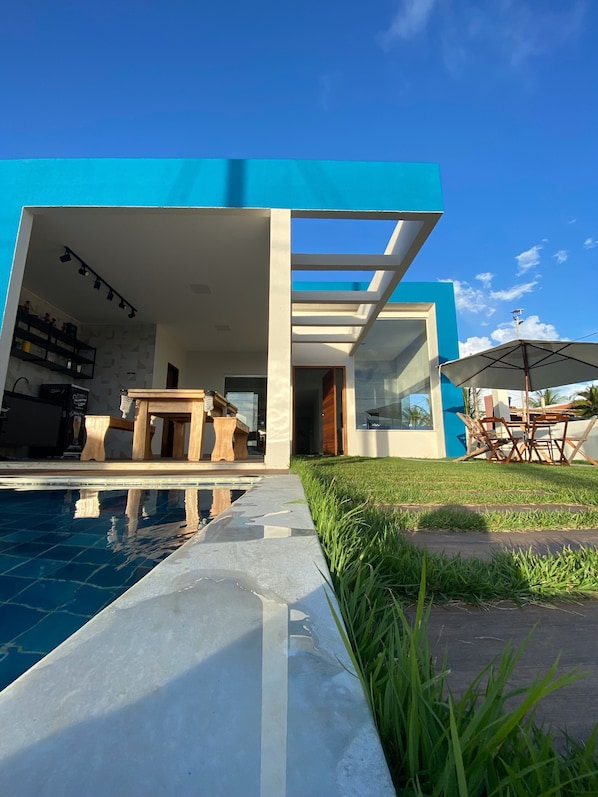 A modern house with a pool, outdoor furniture, and a clear sky.