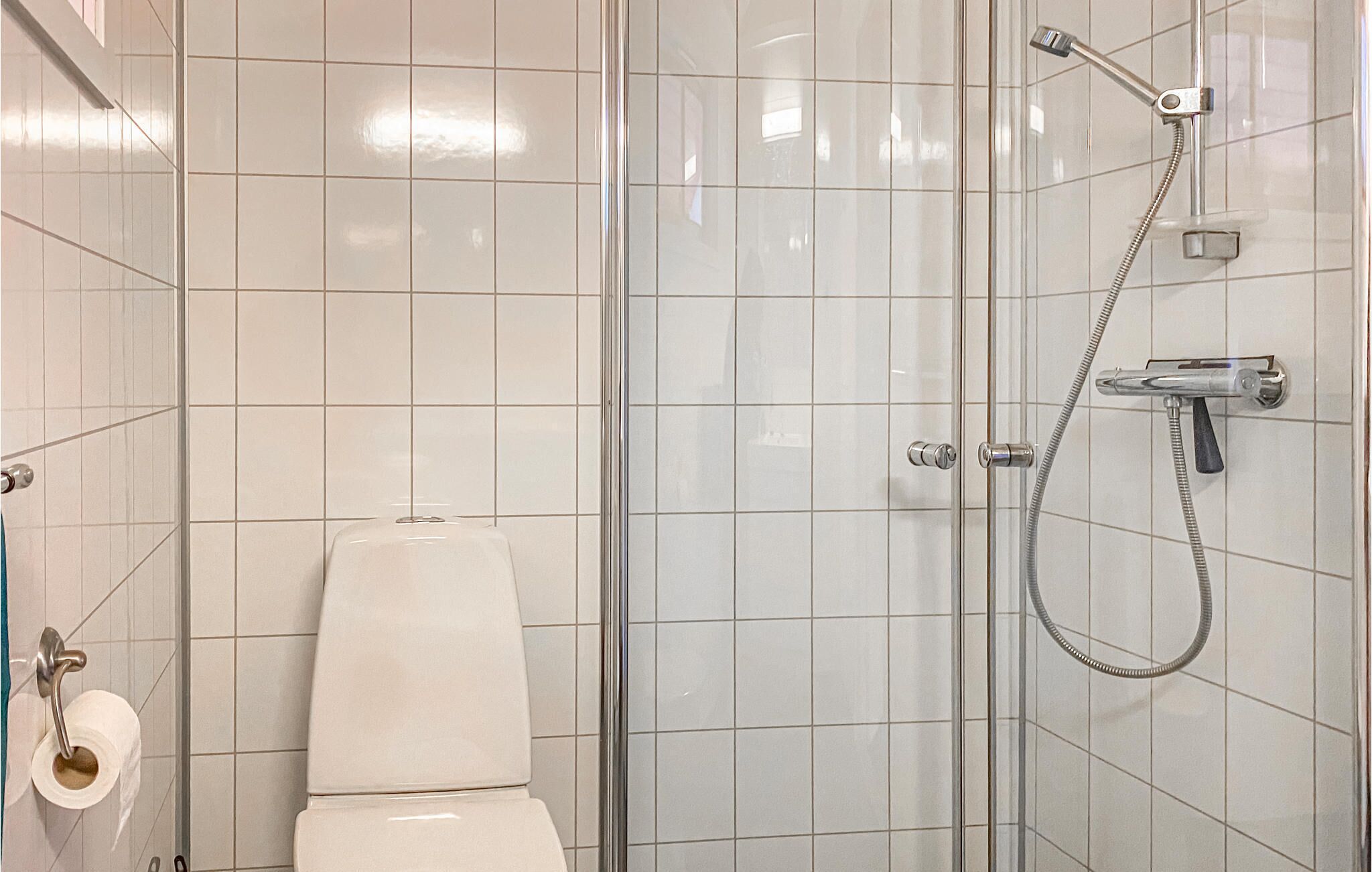 A bathroom with a toilet, a shower with a handheld showerhead, and a toilet paper holder.