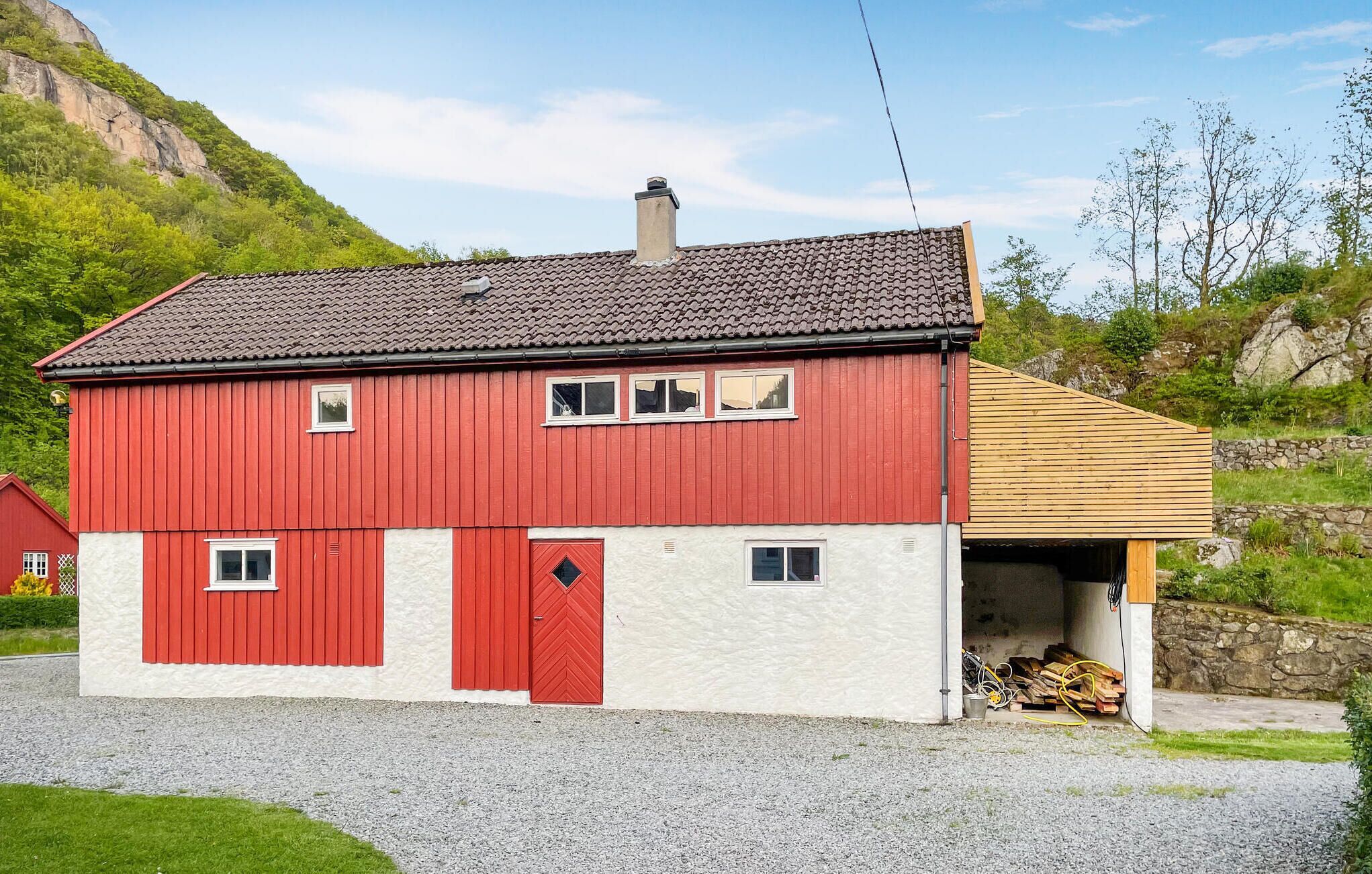 A red and white house with a garage, surrounded by a gravel driveway and greenery.