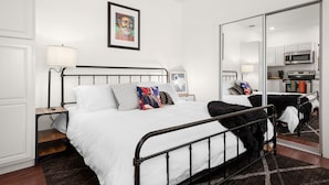 Ein modernes Schlafzimmer mit einem großen Bett, einem Nachttisch, einem Schminktisch und Blick auf eine Küche durch eine Schiebetür.