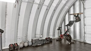 Ein Fitnessstudio mit Trainingsgeräten, darunter Kurzhanteln, ein Ergometer und eine Gewichtbank.
