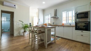 A modern kitchen with white cabinetry, a central island, and a large window providing natural light.