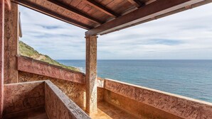 Une vue sur la côte, depuis un balcon en bois, avec la mer en toile de fond et une colline verdoyante.