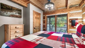 Ein Schlafzimmer mit Holzbalkendecke, einem Bett mit rotem und weißem Quilten, einer hölzernen Kommode, einer Tür und einem Fenster mit Jalousien.