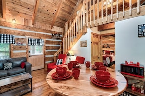 A cozy cabin interior with a wooden ceiling, a dining table set with red dishes, a red sofa, and a red chair.