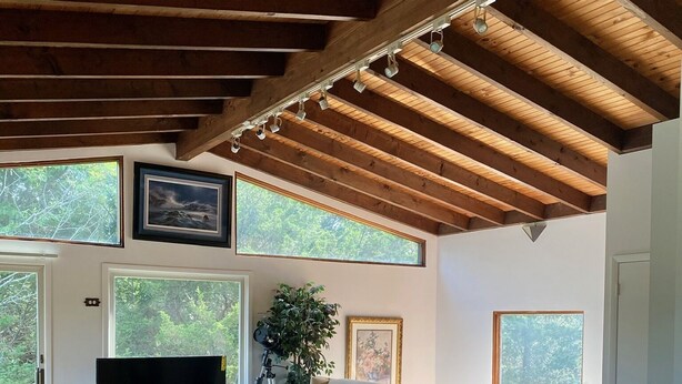 Een ruime woonkamer met een houten plafond, grote ramen, een flatscreen televisie en comfortabele zithoek.